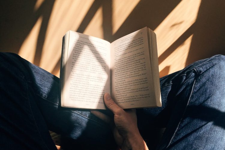 A person reading a book in a softly lit room, with shadows of light across the floor.