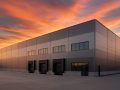 A modern industrial warehouse with loading docks under a colorful sunset sky